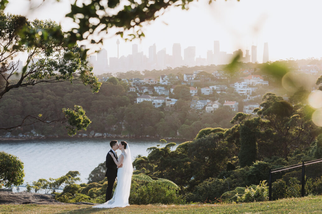 Couple kissing in garden setting with city skyline in the background